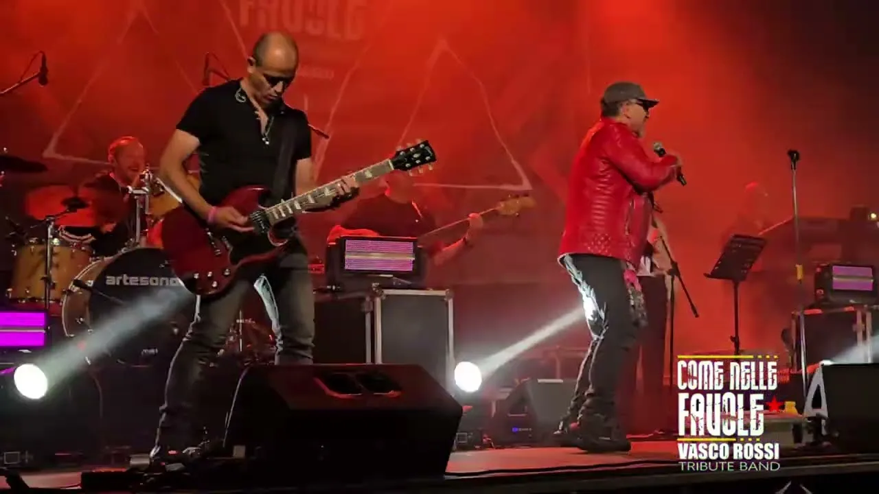 Il chitarrista e il cantante sul palco a Erula, sotto le luci rosse, con batteria e basso alle spalle