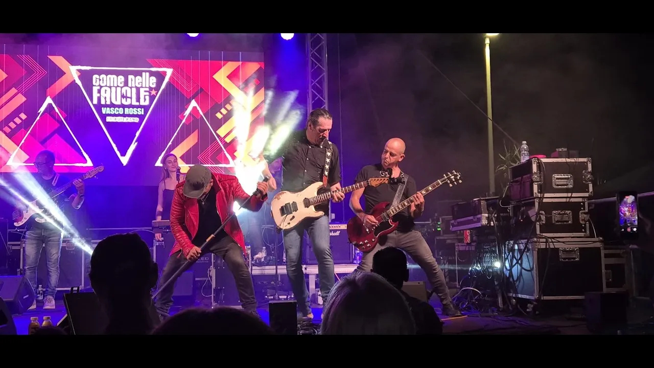 Il cantante col microfono chino in avanti in giacca rossa, con due chitarristi e il bassista alle spalle, davanti al pubblico