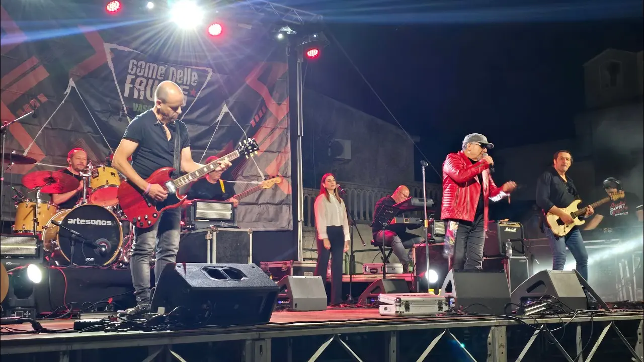 La band al completo sul palco di Erula: chitarra in primo piano, batteria, basso, cori, tastiere e il cantante in giacca rossa al microfono