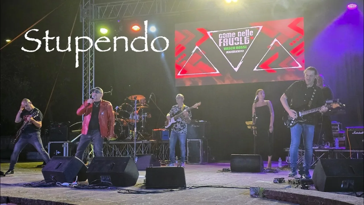 La band al completo sul palco di Isili: il cantante in giacca rossa al microfono, il chitarrista in primo piano, batteria, basso, tastiere e cori sullo sfondo